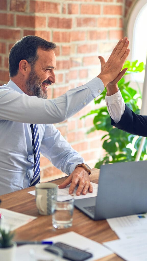 Zwei Geschäftsleute feiern Erfolge mit High Fives in einem Büro während eines Grüntee-Seminars.