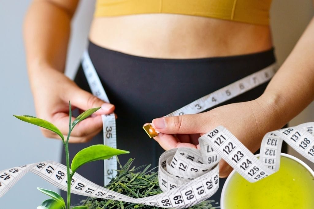 Frau misst Taille mit Maßband - grüner Tee hilft beim Abnehmen und Fettverbrennung
