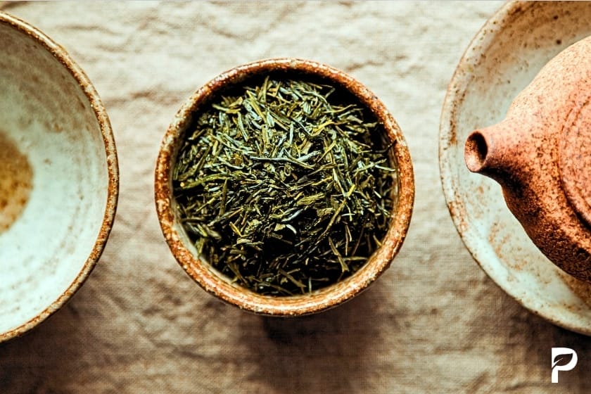 Getrocknete grüne Teeblätter mit hohem Koffeingehalt in traditioneller Keramikschale

