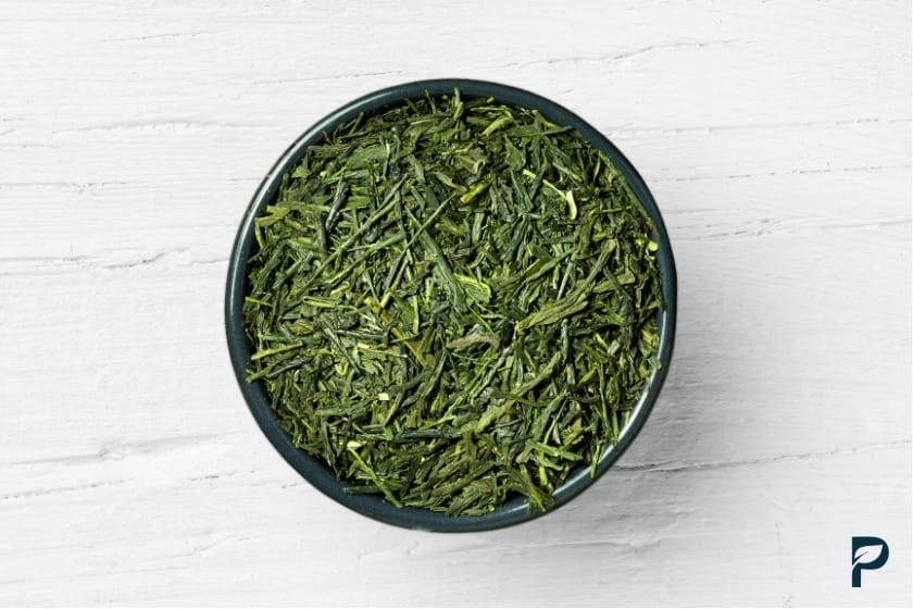 Getrocknete grüner Tee Koffein Blätter in schwarzer Schale auf weißem Holztisch

